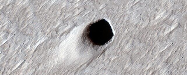A round hole in the grey surface of mars