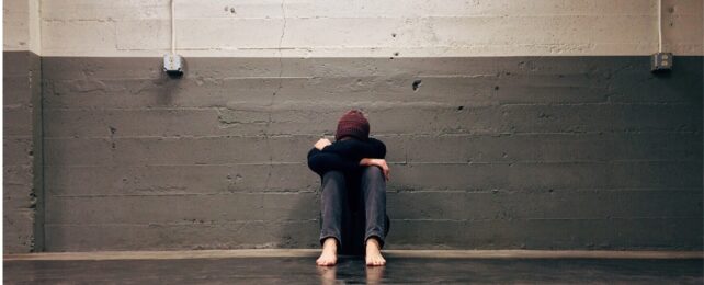 A person sitting against a wall with head resting on arms