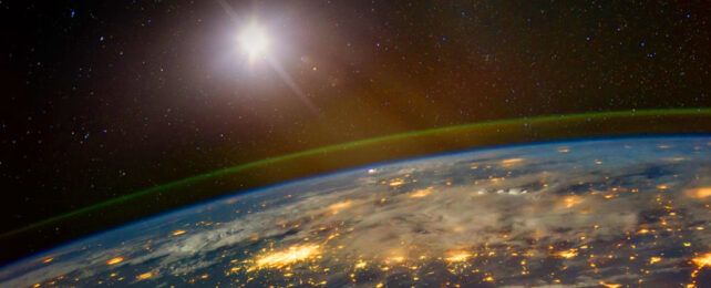 Satellite in orbit reflecting sunlight over night lit cities on earth