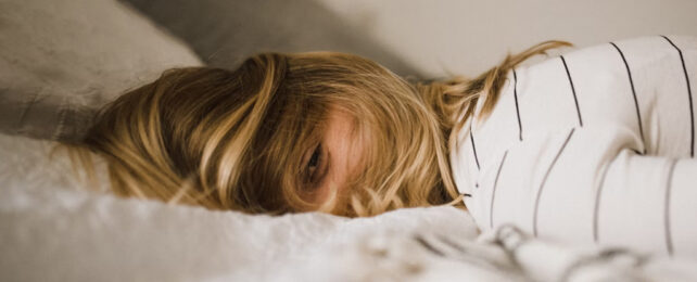 Woman lying on stomach in bed, eye peeking out between hair over face