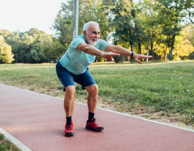 An older male squatting with outstretched arms in a park 