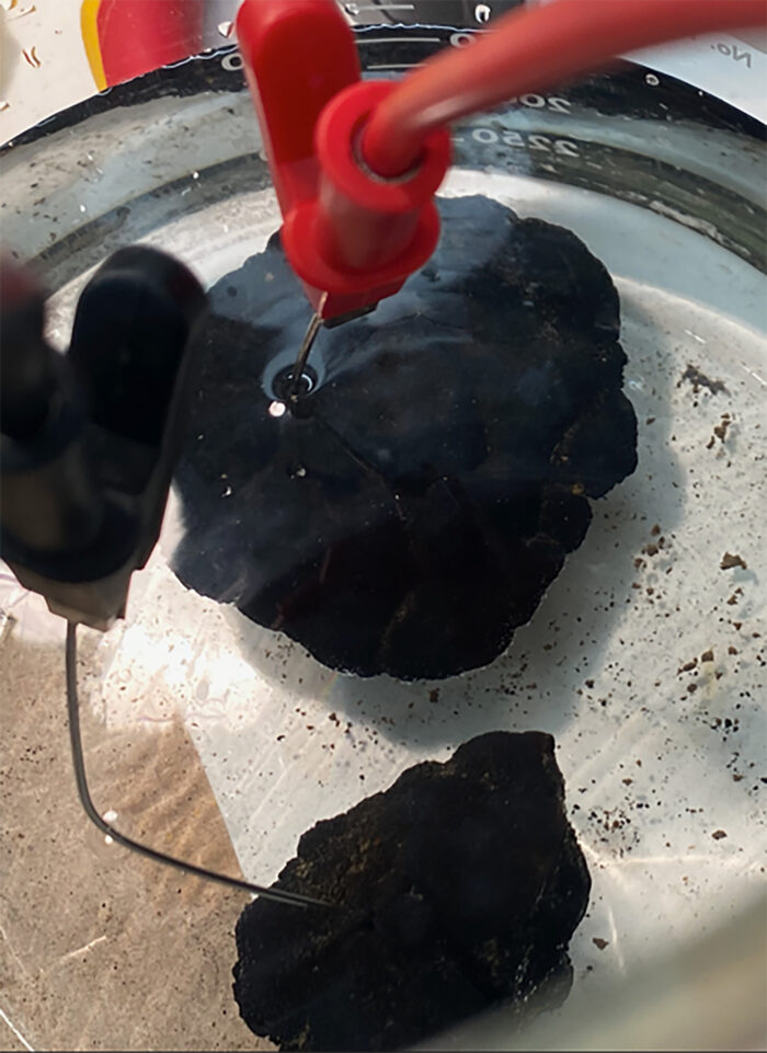 pitch black wet rock being probed in lab