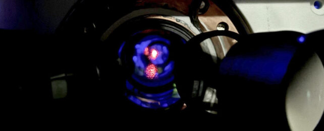 Close up of pink-colored laser beam inside lab instrument.