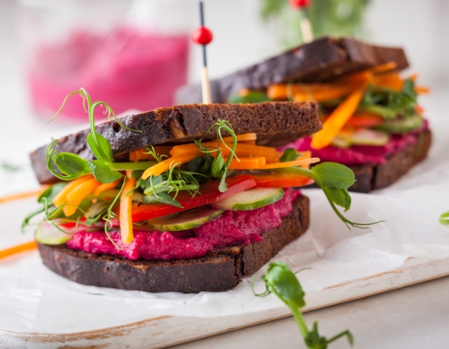 Two sandwiches on rye bread with bright colored vegan fillings