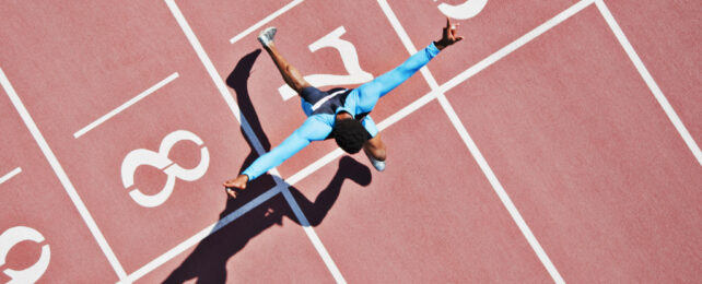 Aerial view of runner in blue crossing white finish line on red track