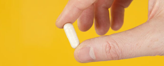 hand holding a white pill on yellow background