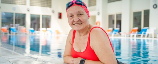 An older lady in a red swimsuit leaning on the edge of a swimming pool