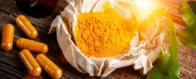 Powdered tumeric in a bowl with capsules next to it