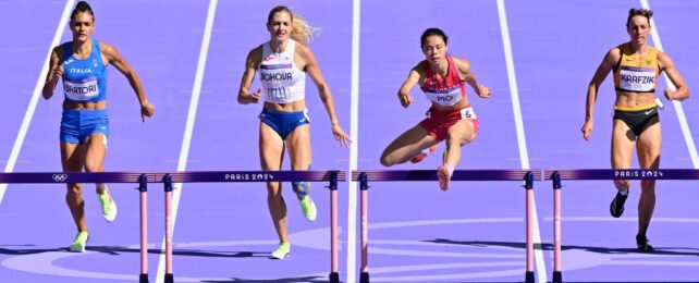 Four women competing in hurdles on a purple track