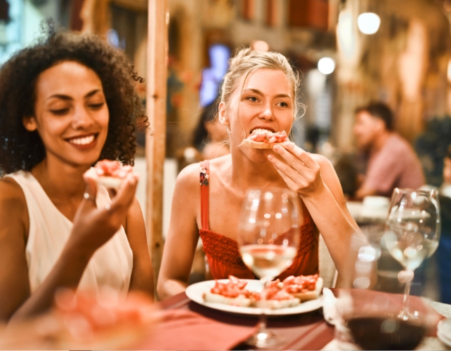 Two young women eating pizza and drinking wine