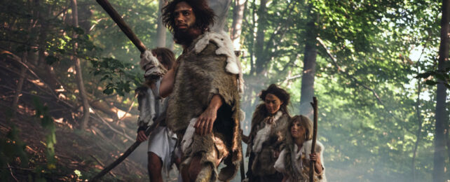 Small group of people in furs with wooden hunting tools walking through a forest