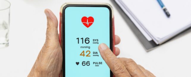 A smartphone screen showing blood pressure readings, being held by elderly hands