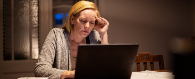 A women with shoulder length auburn hair sitting in front of a laptop in dim light