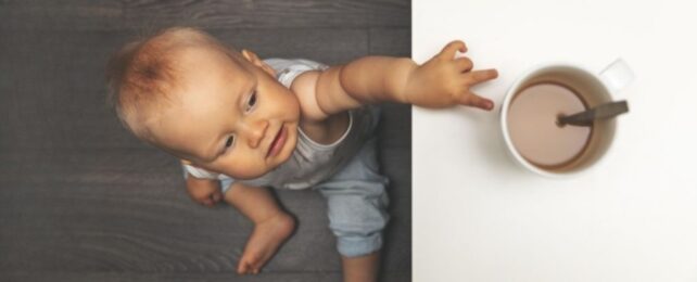 Baby from above reaching up to coffee mug on table