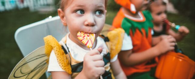 Child in a bee costume sucking a colorful lollypop