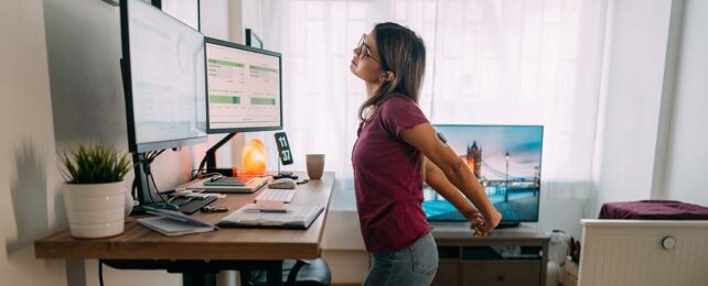 woman in work from home office at a standing desk, stretching her arms