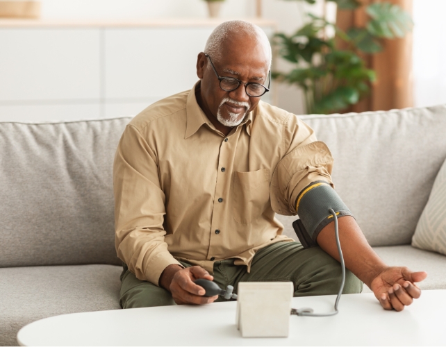 A man sitting on a couch taking his blood pressure 