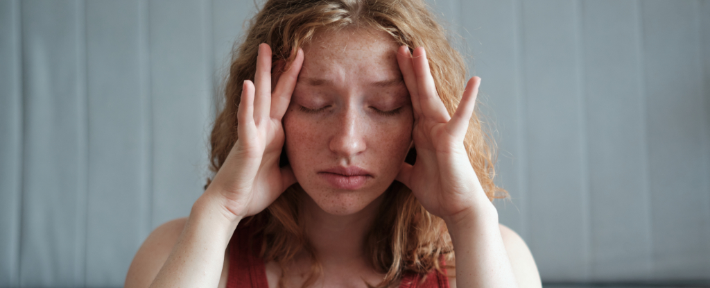 red haired woman holding her head with eyes closed