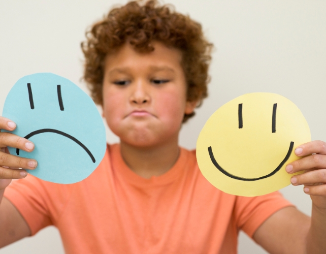 A child holding drawn smiling and sad faces