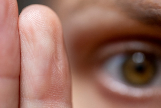 An eye with two fingers in the foreground