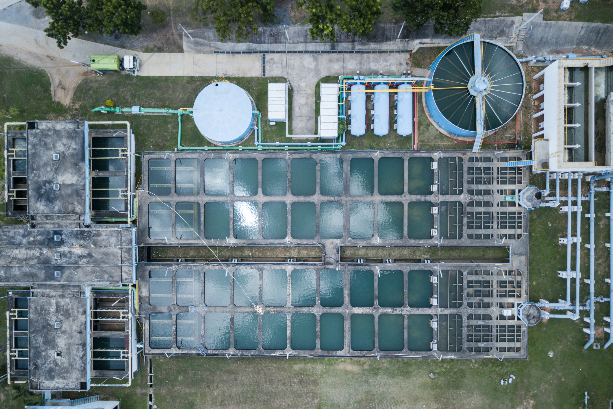 An aerial view of a water treatment plant, showcasing the complex infrastructure involved in providing clean water. The image features multiple rectangular tanks filled with water, a circular filtration tank, and various pipes and equipment.