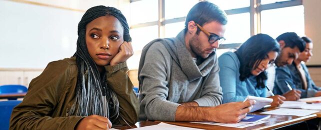 a row of university students focused on work. a woman in the foreground is distracted, looking sideways.