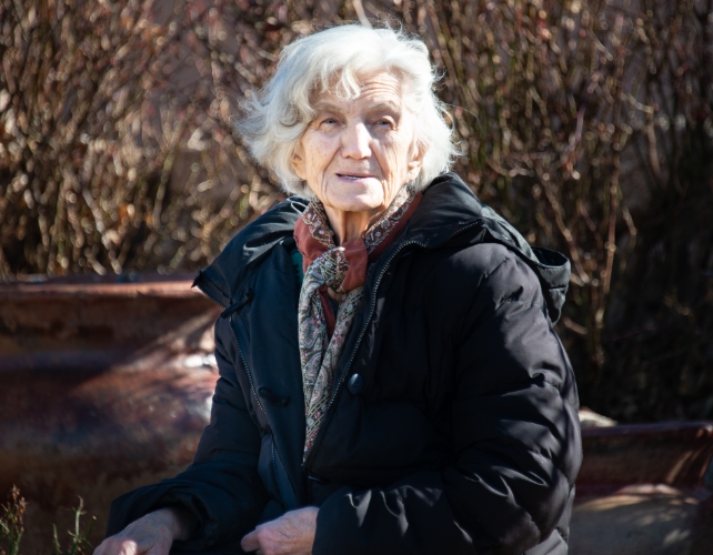 An older lady in a black jacket sitting outdoors