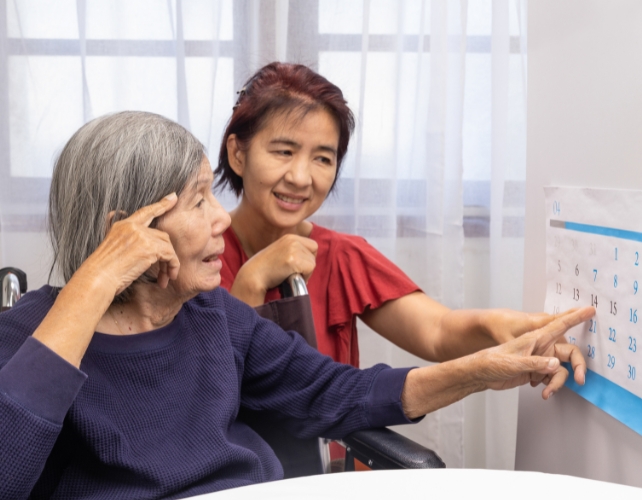 Older woman in a wheelchair pointing to a calendar to a middle-aged woman