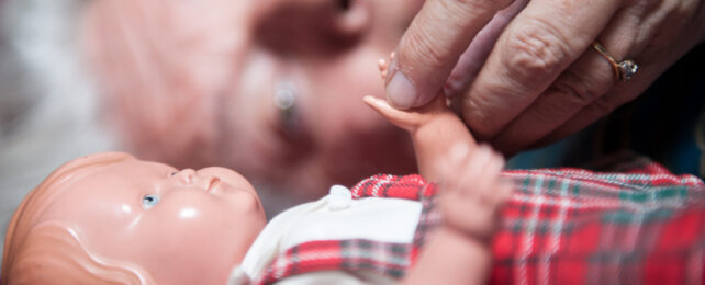 older person laying next to a doll, holding its hand