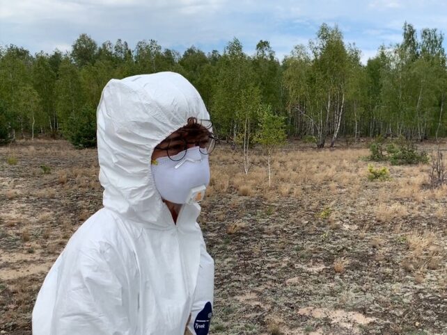 A person wearing PPE, standing in a field