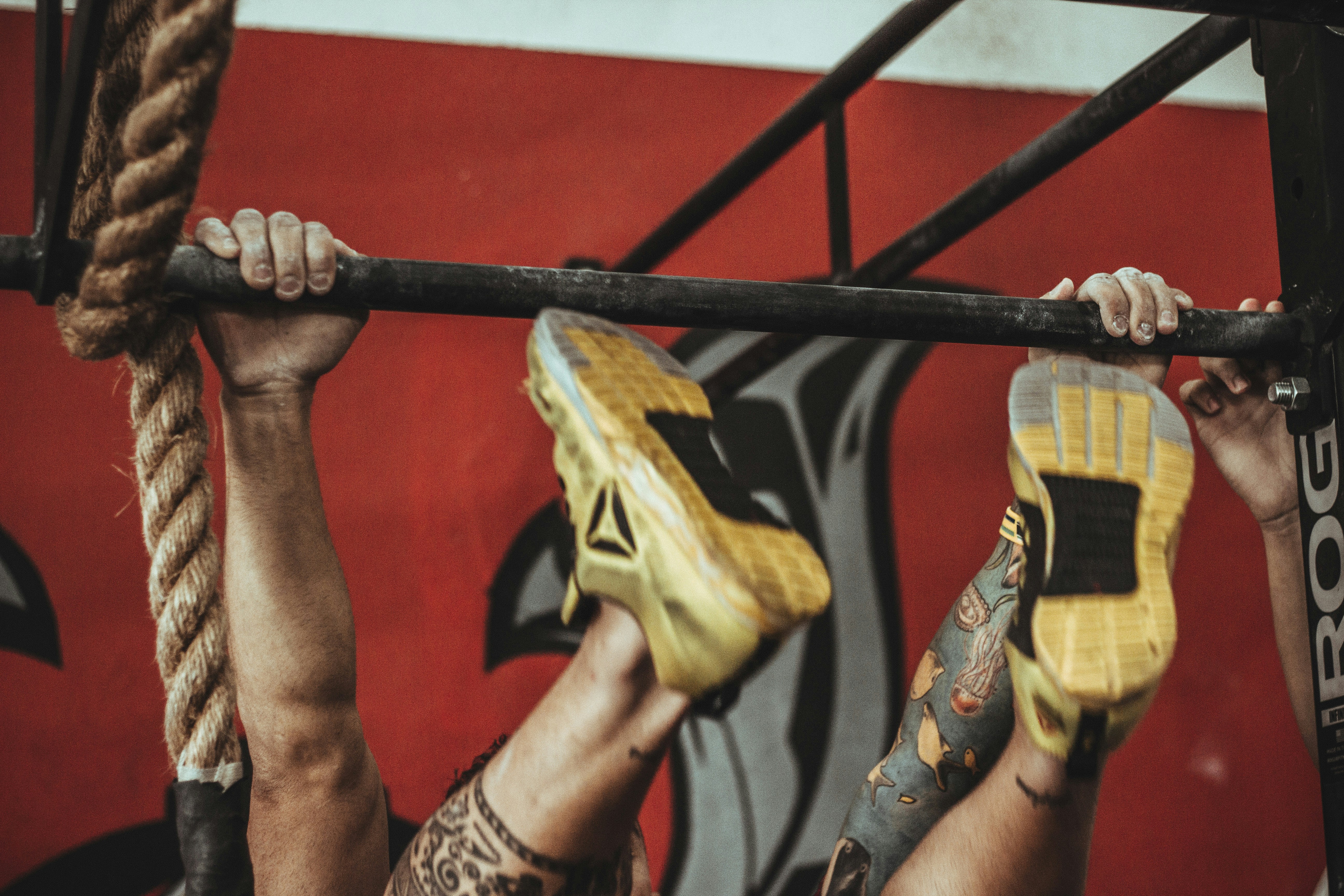 person wearing yellow-and-black Reebok low-top athletic shoes hanging on pull-up bar