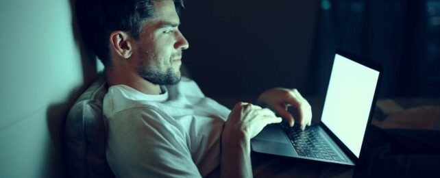 Man in bed bathed in green light from laptop screen