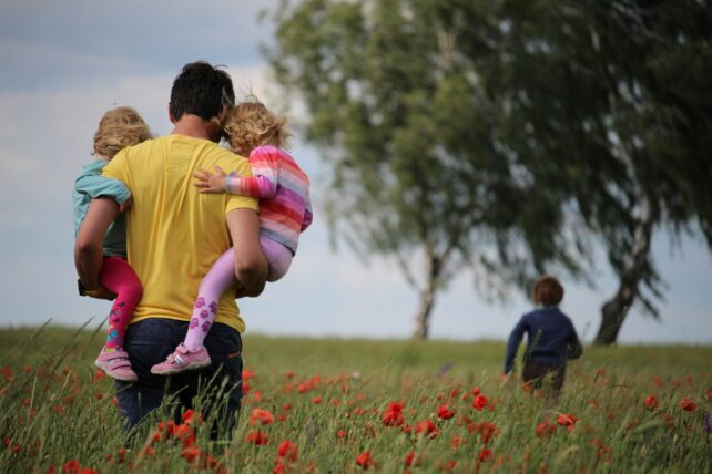 Man holding two similar sized children in a field