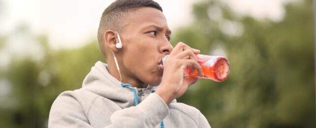 Man outside in hoodie drinking red drink