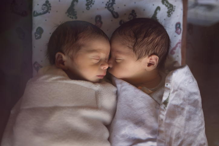 Premature newborn twins sleeping together in a hospital crib