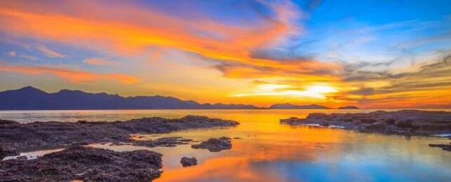 Sea and sky stained orange amidst blue at sun set