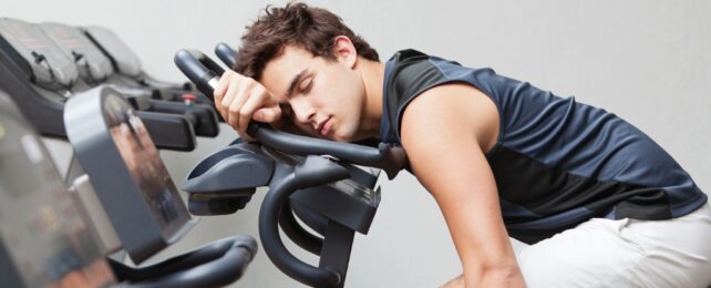 A young man asleep leaning on an exercise bike