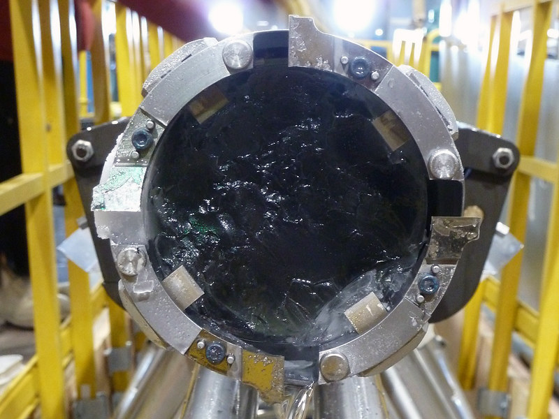 looking down the barrel of an industrial-looking metal tube full of ice, with yellow industrial metal shapes in the background