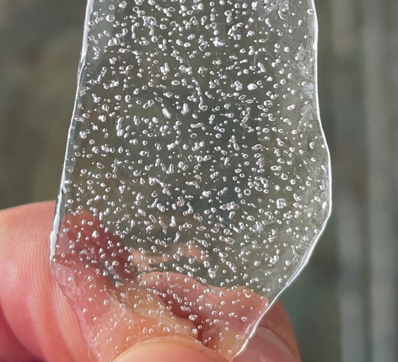 a shard of ice containing many tiny bubbles is in a person's hand