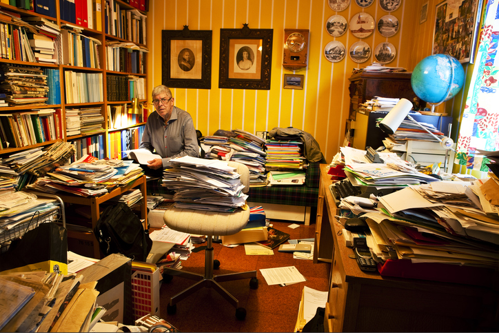 Older man sitting in a room full of paper piles