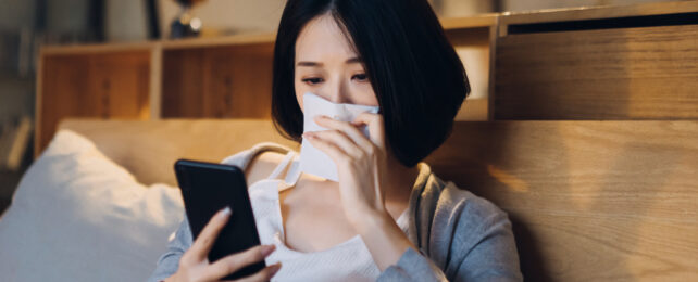 woman with tissue on her nose, looking at her phone