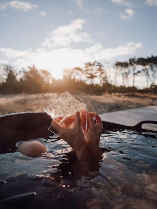 Hands emerging from water in outside tub holding two shards of ice