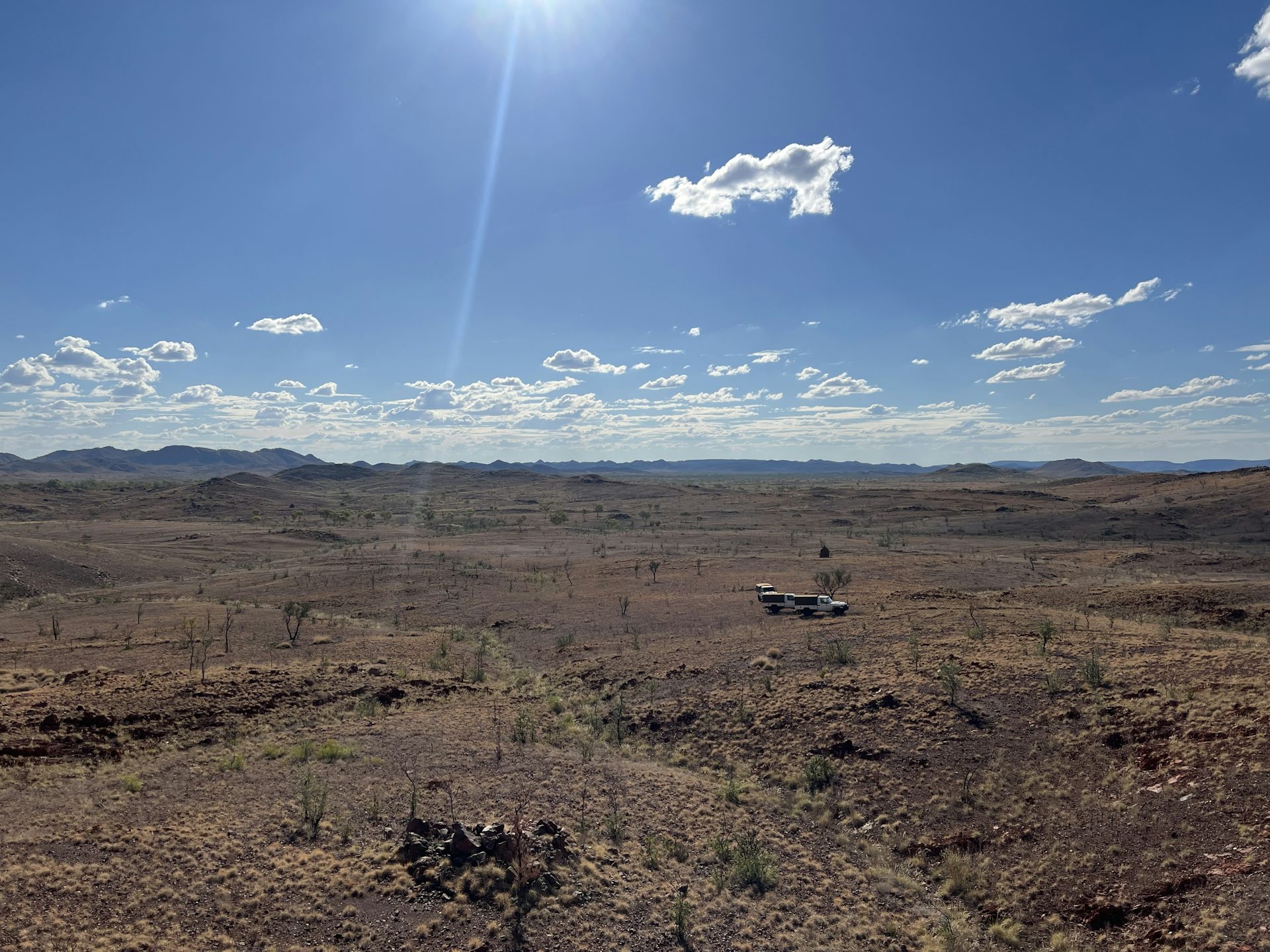 Sparsely vegetated, dry, open landscape with distant small hills under cloud studded blue sky