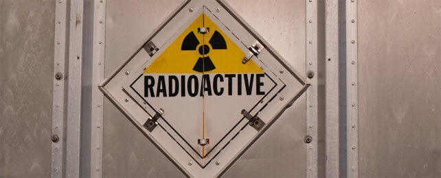 A Bright yellow and black radioactive warning symbol known as a Trefoil on the back of a stainless steel truck trailer.